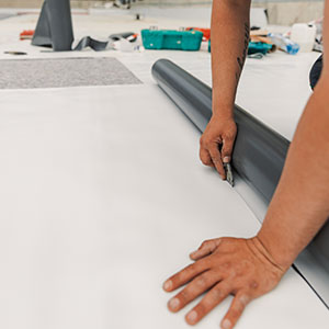 Close up of a worker cutting off a piece of a single-ply sheet from a roll