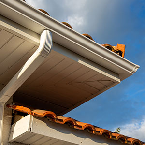 Bottom up view of a gutter system alongside a residential roof with orange clay tiles
