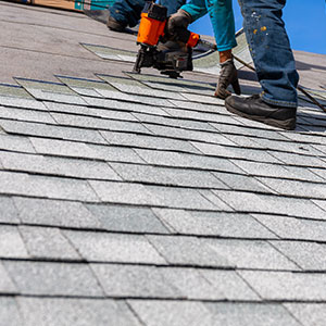 Close up of a worker installing gray shingles on a residential roof with a nailgun