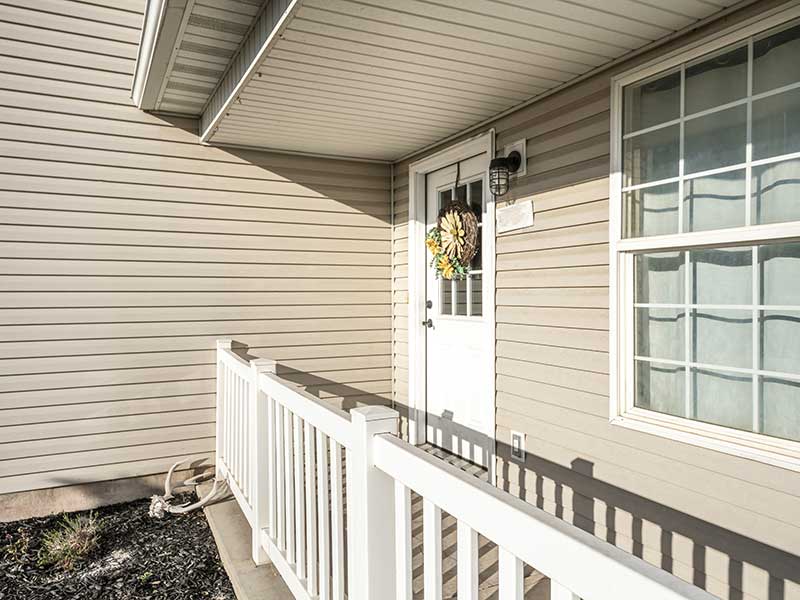 Close up of a front porch with a front door and window and beige vinyl siding